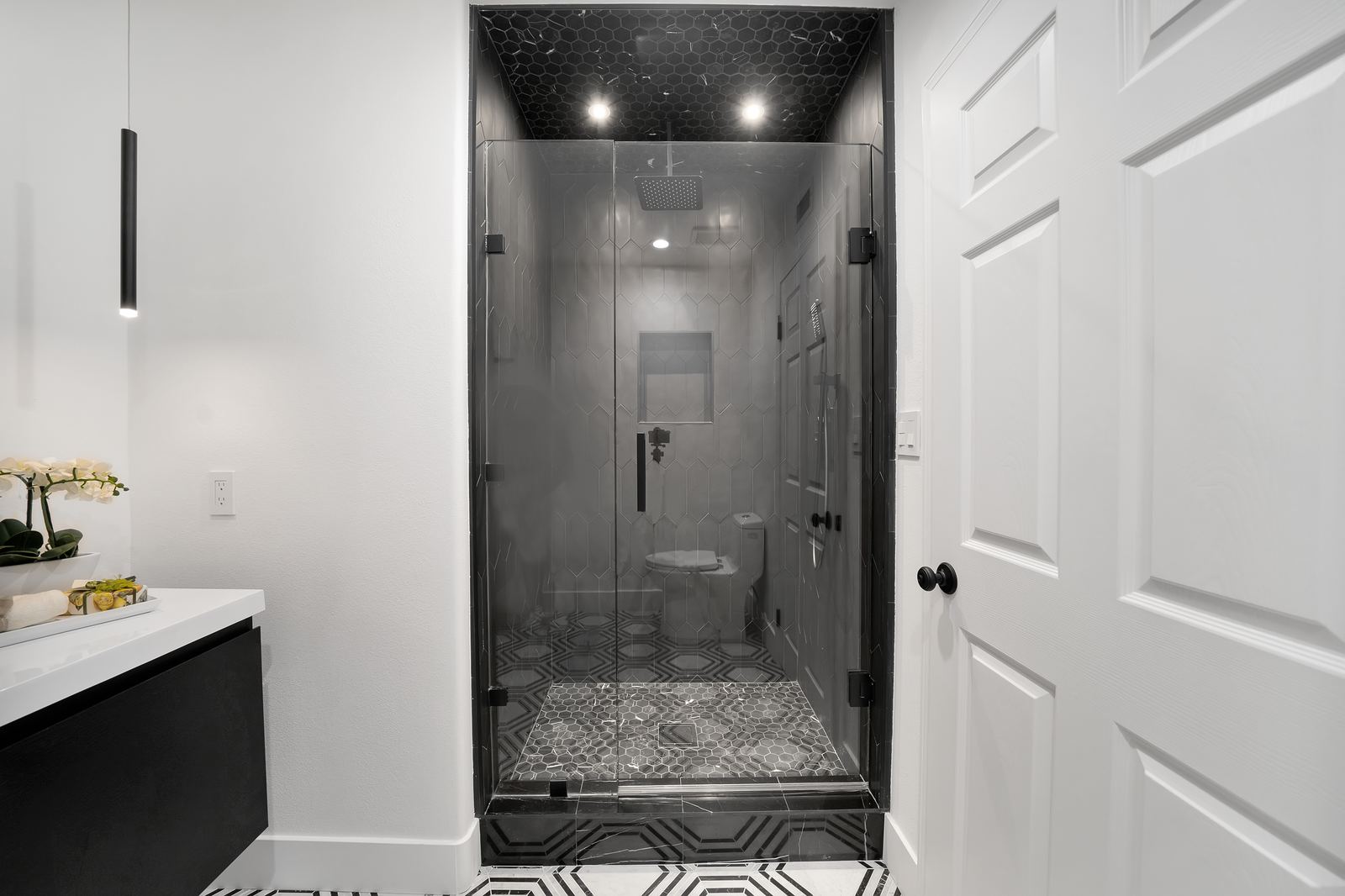 Custom shower remodel with black marble hexagon tile ceiling and floor, frameless glass door