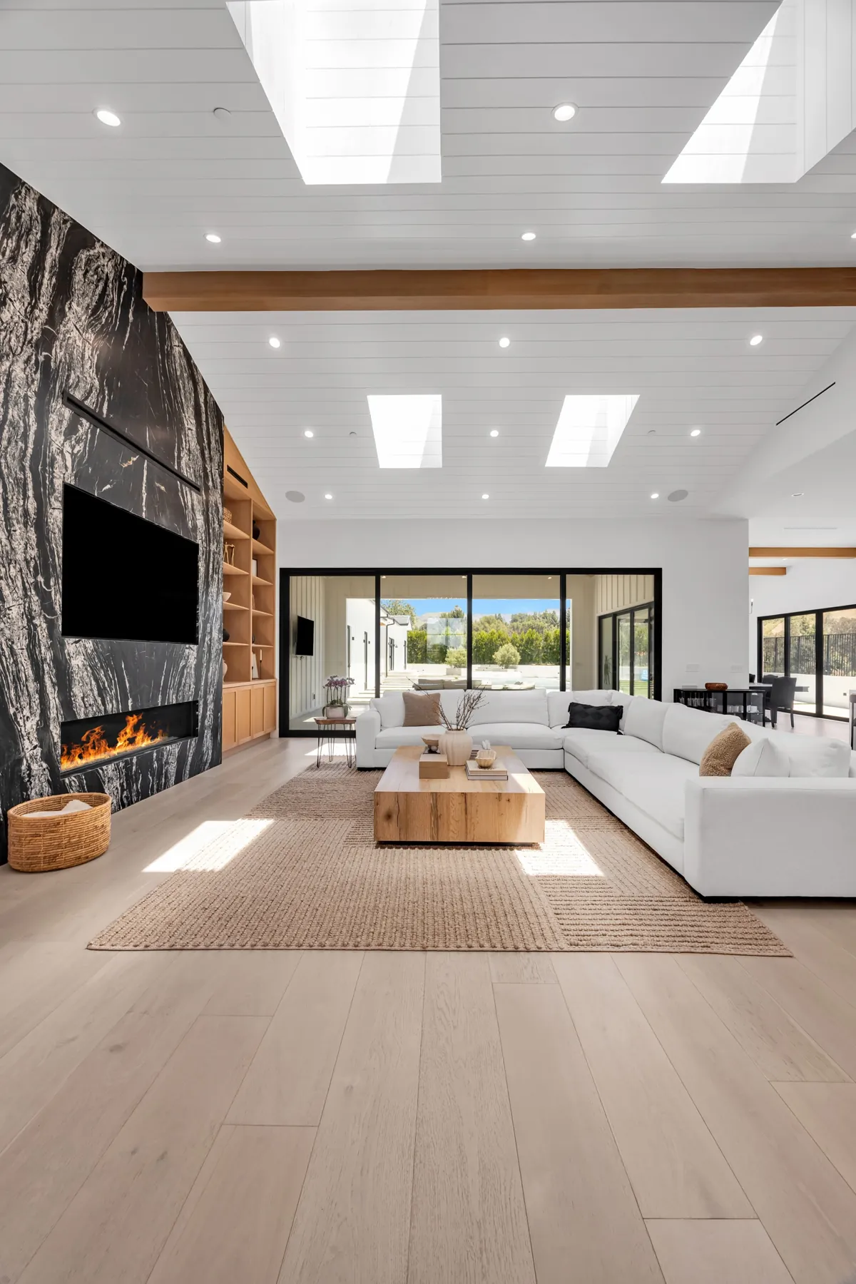 Living room with light white oak floors running toward tall windows