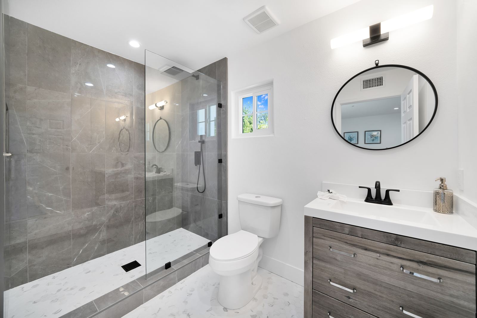 Shower remodel with large gray porcelain tile, fixed glass panel and hexagon mosaic shower floor